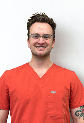 Dr. Cody Riffe smiles for a professional headshot in front of a white background. He is wearing orange scrubs.