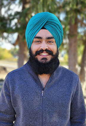 Dr. Talwinder Dhanjal smiles outside for a professional headshot. He's wearing a navy sweatshirt and a teal dastār (Sikh headwrap for men).