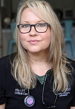 Veterinary technician Ally Dearth smiles while wearing black scrubs and a stethoscope around her neck.