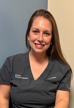 Shannon Scheitle smiles in an exam room in our hospital. She is wearing dark grey scrubs embroidered with the BluePearl logo.