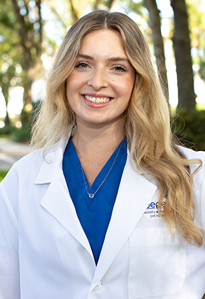 Dr. Kaitlyn Cassel smiles outside for a professional headshot. She is wearing blue scrubs and her BluePearl whitecoat.