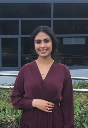 Dr. Nikisha Dheendsa smiles outside of a veterinary school building. She is wearing a maroon dress.