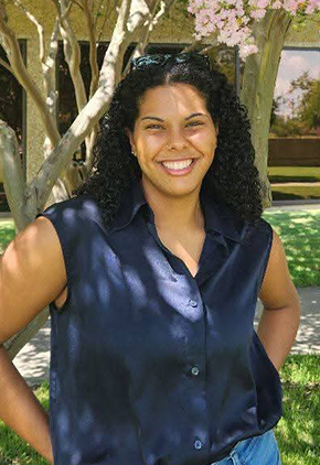 Dr. Elvena Baptiste smiles outside for a professional photo. She is wearing a navy-blue blouse and blue jeans.