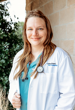 Dr. Jessica Krebs smiles outside for a professional headshot. She has on light teal scrubs, her BluePearl white coat and has her stethoscope around her neck.