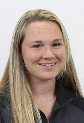 Dr. Avery Karich smiles for a professional headshot in front of a white background. She is wearing a black and grey athletic jacket.
