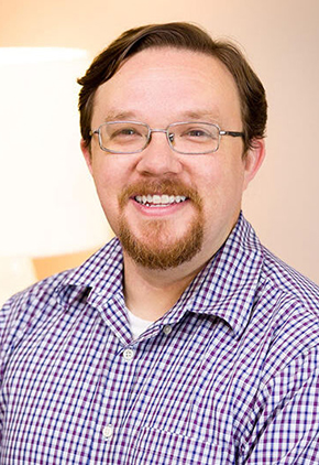 Dr. James Pendergraft smiles for a professional headshot. He is wearing a blue checkered shirt and rectangle glasses.