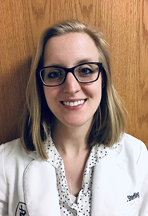 Dr. Sarah Sterling smiles for a professional photo. She is wearing her whitecoat and black oval glasses.