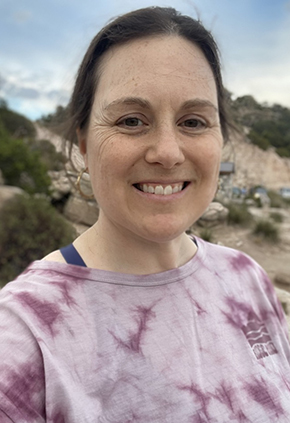 Dr. Lindsey Schneider smiles outside while on a hike. She has on a mauve tie-dyed shirt.