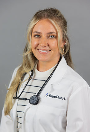 Dr. Arden Tiffee smiles for a professional headshot in front of a grey background. She is wearing a white shirt with black stripes, her BluePearl white coat and a stethoscope around her neck.