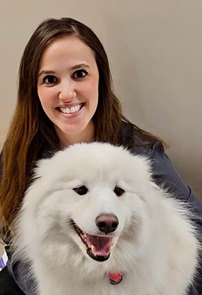 Dr. Olivia Thaw smiles in front of a beige wall with her Great Pyrenees in her lap.