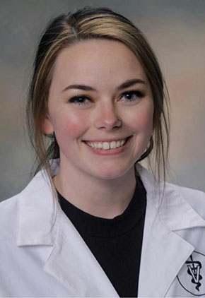 Dr. Bailey Hallgren Meehan smiles for a professional headshot in front of a light greyish background. She is wearing her veterinary school white coat.