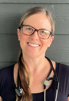Dr. Kelly Gavin smiles for a headshot in front of the side of a building. She is wearing a black top and has a black stethoscope around his neck.