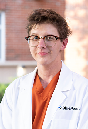 Dr. Faurest Nelson Wicks smiles outside for a professional headshot. He is wearing orange scrubs and his BluePearl whitecoat.