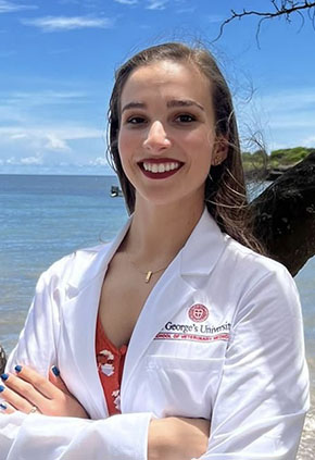 Dr. Samantha Forjan smiles on the beach in Grenada. She is wearing her St. George University white coat.