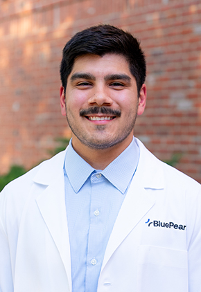Dr. Yan Zermeno smiles outside in front of a brick building. He is wearing a light blue dress shirt and his BluePearl whitecoat.