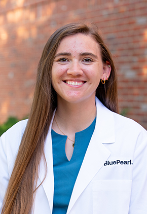 Dr. Rachel Brungardt smiles outside in front of a brick building. She is wearing a blue blouse and her whitecoat.