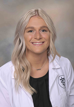 Dr. Kylie Levan smiles for a professional headshot. She is wearing a black top and her school white coat.