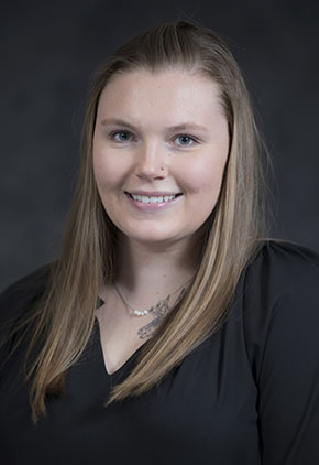 Dr. Justine Finerty smiles for a professional headshot in front of a black studio backdrop. She is wearing a black blouse.