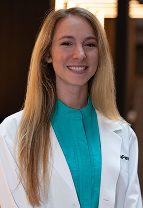 Dr. Grace Johnston smiles for a headshot in the lobby of BluePearl Pet Hospital. She is wearing a turquoise blouse and her whitecoat.