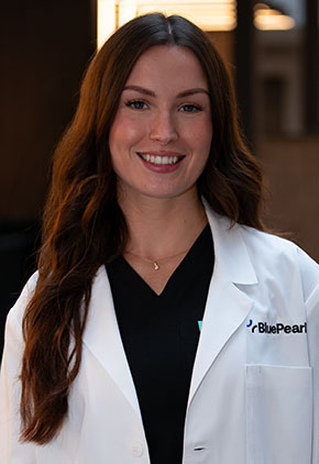 Dr. Rebecca Wassmuth smiles for a headshot in the lobby of BluePearl Pet Hospital. She is wearing black scrubs and her whitecoat.