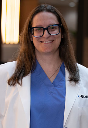 Dr. Virginia Womack smiles for a headshot in the lobby of BluePearl Pet Hospital. She is wearing blue scrubs and her whitecoat.