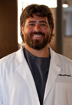 Dr. Cristhian Marques smiles for a headshot in the lobby of BluePearl. He is wearing a grey top and his whitecoat.