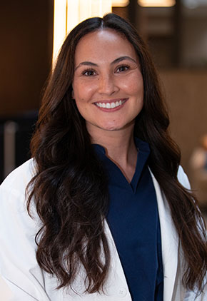 Dr. Bianca Coleman smiles for a headshot in the lobby of BluePearl Pet Hospital. She is wearing navy scrubs and her whitecoat.