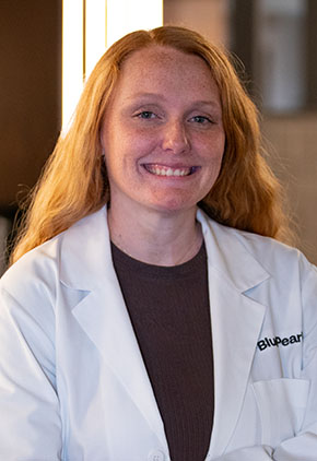 Dr. Katherine Green smiles for a headshot in the lobby of BluePearl Pet Hospital. She is wearing a maroon top and her whitecoat.