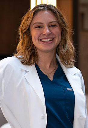 Dr. Samantha Higgins smiles for a headshot in the lobby of BluePearl. She is wearing royal blue scrubs and her whitecoat.
