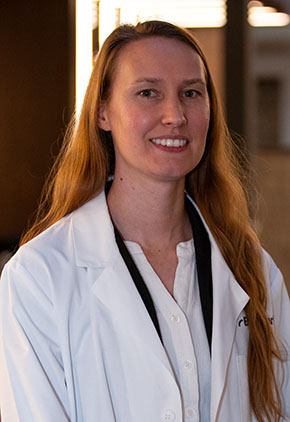 Dr. Kellie Holden smiles for a headshot in the lobby of BluePearl Pet Hospital. She is wearing a white blouse and her whitecoat.