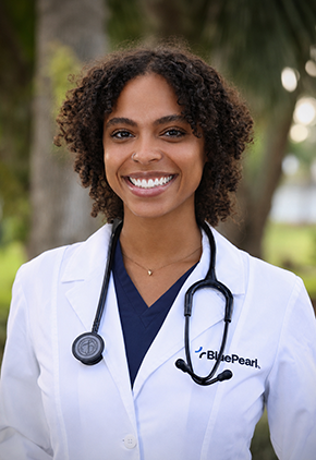 Dr. NaaLamiley Kwakye smiles outside for a professional headshot. She is wearing navy scrubs and her BluePearl whitecoat with a stethoscope around her neck.