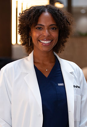Dr. NaaLamiley Kwakye smiles for a headshot in the lobby of BluePearl Pet Hospital. She is wearing navy scrubs and her whitecoat.