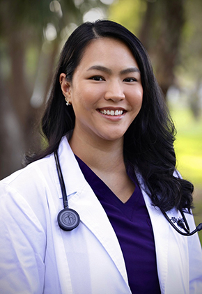 Dr. Jennifer Maharath smiles outside for a professional headshot. She is wearing purple scrubs, her BluePearl whitecoat and has a stethoscope around her neck.