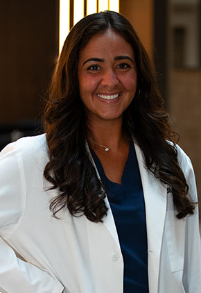 Dr. Christiana Popo smiles for a headshot in the lobby of BluePearl Pet Hospital. She is wearing navy scrubs and her whitecoat.