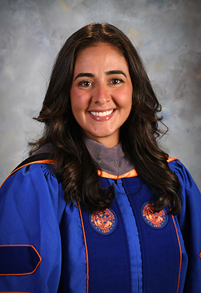 Dr. Christiana Popo smiles for a professional graduation photo in front of a grey background. She is wearing her University of Florida doctoral robes.