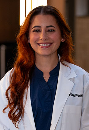 Dr. Amanda Rosendo Ocasio smiles for a headshot in the lobby of BluePearl Pet Hospital. She is wearing a navy blouse and her whitecoat.