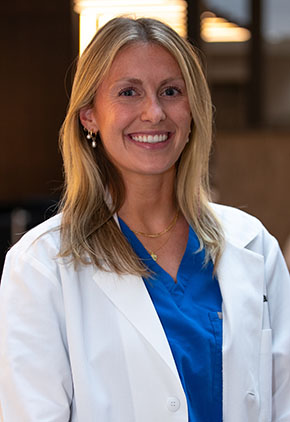 Dr. Anabelle Wondrasch smiles for a headshot in the lobby at BluePearl Pet Hospital. She is wearing royal blue scrubs and her whitecoat.