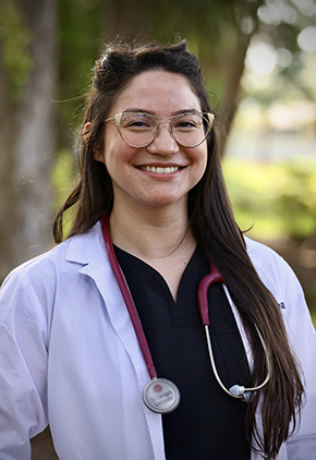 Dr. Daniela Yarrington smiles outside for a professional headshot. She is wearing a black blouse, her BluePearl whitecoat and has a magenta stethoscope around her neck.