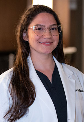 Dr. Daniela Yarrington smiles for a headshot in the lobby of BluePearl Pet Hospital. She is wearing a black blouse and her whitecoat.