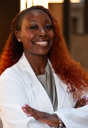 Dr. Morgan Banks smiles for a headshot in the lobby of BluePearl Pet Hospital. She is wearing a silver blouse and her whitecoat.