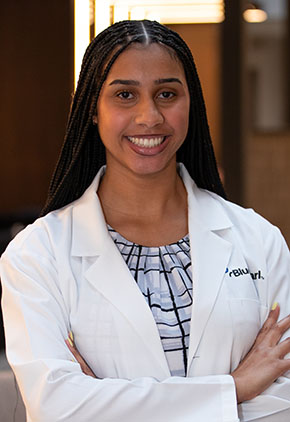 Dr. Kierney Burks smiels for a headshot in the lobby of BluePearl Pet Hospital. She is wearing a white shirt that features a black webbing pattern and her whitecoat.