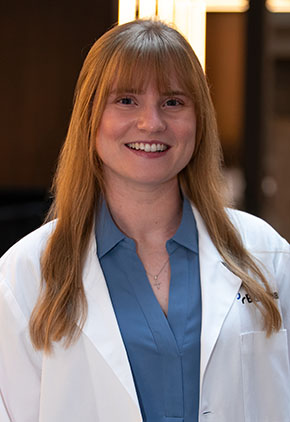 Dr. Emilee Roberts smiles for a headshot in the lobby of BluePearl Pet Hospital. She is wearing a smoky blue blouse and her whitecoat.