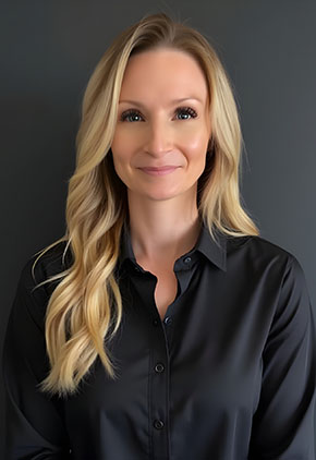 Dr. Lindsey Wicks smiles for a professional headshot in front of a black background. She is wearing a black collard blouse.