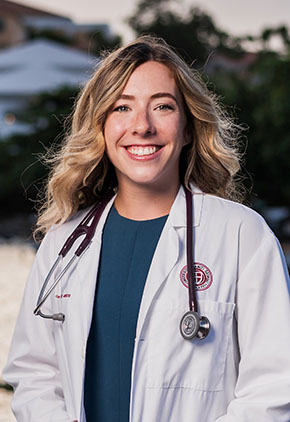 Dr. Kyra Boss smiles outside on campus in her St. George's University whitecoat.