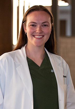 Dr. Brittany Anglin smiles for a headshot in the lobby of BluePearl Pet Hospital. She is wearing olive green scrubs and her whitecoat.