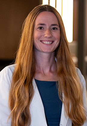 Dr. Anne Seyfried smiles for a headshot in the lobby of BluePearl Pet Hospital. She is wearing a navy blouse and her whitecoat.
