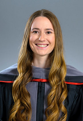 Dr. Anne Seyfried smiles for a studio photo in front of a grey backdrop. She is wearing her doctoral robe.