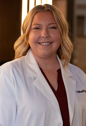 Dr. Nicole Nelson smiles for a headshot in the lobby of BluePearl Pet Hospital. She is wearing a maroon blouse and her whitecoat.