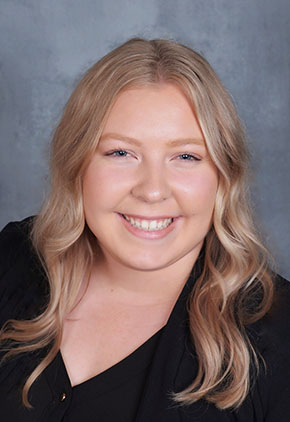 Dr. Nicole Nelson smiles for a professional headshot in front of a blue-grey studio backdrop. She is wearing a black blouse.