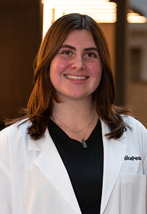 Dr. Danielle Alms smiles for a headshot in the lobby of BluePearl Pet Hospital. She is wearing a black top and her whitecoat.